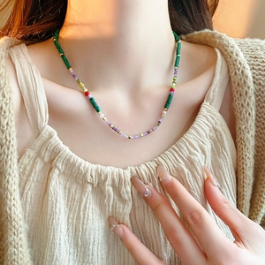 Detail of a handmade beaded necklace with green, purple and red beads on a model