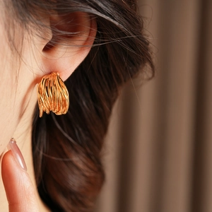 Macro shot of gold-plated multi-layer intertwined C-shaped earrings on model