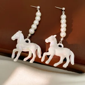 Elegant beaded pearl earrings with iridescent white horse pendant on dark jewelry box