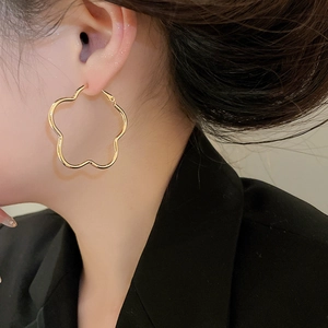 Detailed close-up of gold flower-shaped hoop earrings worn by a model in profile
