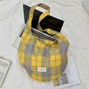 Détail macro d'un sac hobo en toile à carreaux jaunes posé sur un ordinateur portable