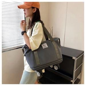 Gray expandable travel bag with wheels and shoulder strap shown in a lifestyle setting