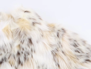 Close-up of soft off-white faux fur texture with dark brown spots on the coat fabric