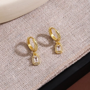 Close-up of golden rectangular drop earrings with brilliant cubic zirconia halo setting