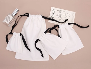 Detailed view of four cream cotton drawstring pouches in various sizes with black ribbons