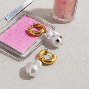 Close-up of gold hoop earrings with white pearls and small colored gemstones details