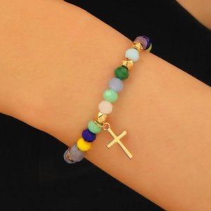 Close-up of a colorful beaded bracelet with a minimalist gold cross pendant on a wrist