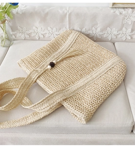 Detailed macro view of large woven straw tote bag with elegant tassel bead charm