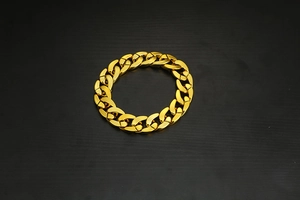 Detailed top view of a chunky gold-colored plastic Cuban chain bracelet on black background