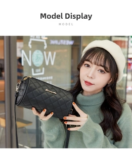Quilted cylinder shoulder bag in black faux leather worn by a model in a green sweater