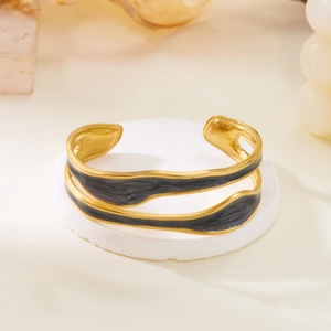 Detail of minimalist wave-shaped gold cuff bracelet with dark grey marble enamel inlay