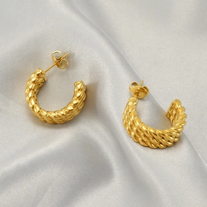 Golden woven twisted hoop earrings in C-shape on elegant white silk fabric background