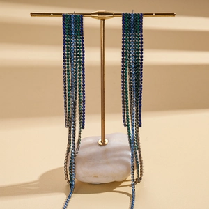 Close-up of long tassel earrings with blue and green rhinestones on a gold display stand