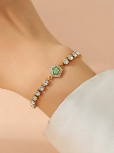 Close-up of golden rhinestone chain bracelet with a pentagon green gemstone charm