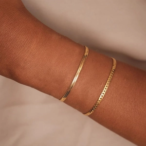 Gros plan de bracelets chaîne serpent et gourmette dorés superposés sur le poignet