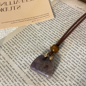 Detail of purple square gemstone pendant with brown leather cord on vintage book