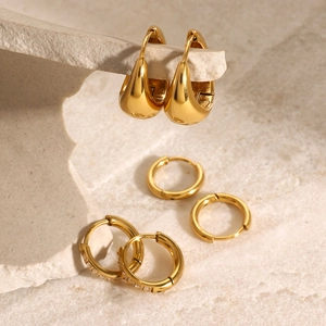 Close-up of golden stainless steel hoop earrings with cubic zirconia on stone background