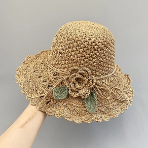 Detailed close-up of handmade straw hat featuring woven flower and green leaf accents