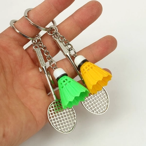 Close-up of hand holding silver badminton racket keychain with green and yellow shuttlecocks