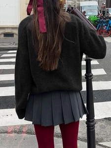 Rear view of model in dark green knit sweater and pleated skirt on city street