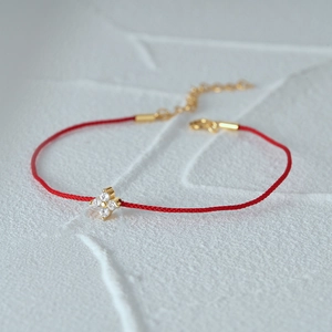 Detail of red braided string bracelet with gold flower pendant and clear zircon stones