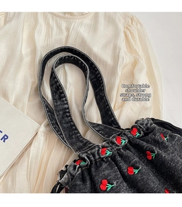 Detail of cherry embroidery on black denim bucket bag with wide comfortable strap