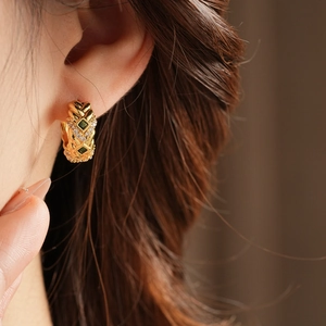 Detail of vintage gold hoop earring featuring a green square zircon and small diamonds