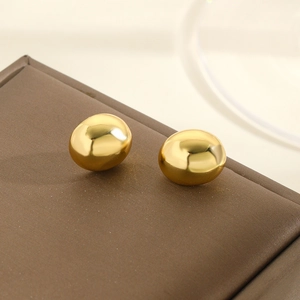Macro shot of polished gold-plated bean-shaped stud earrings on a brown leather texture