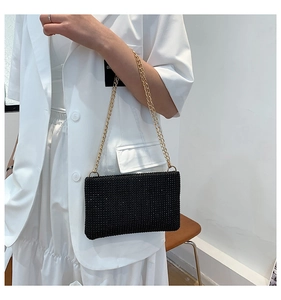 Detail of elegant black rhinestone evening bag with double gold chain on white suit