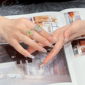 Close-up of gold and silver flower rings with green stones on elegant manicured hands