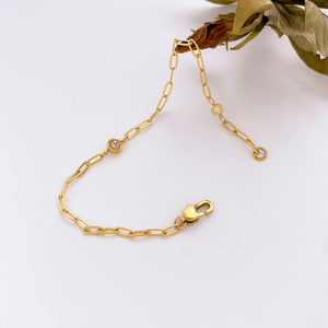 Close-up of golden link chain bracelet featuring a round gemstone and lobster clasp detail