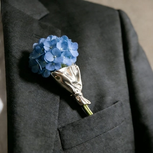 Detail einer künstlerischen blauen Hortensien-Brosche an grauer Sakkotasche