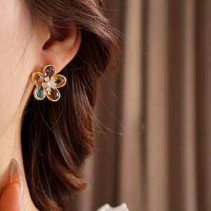 Close-up of elegant gold floral stud earring with colorful zircon stones on model