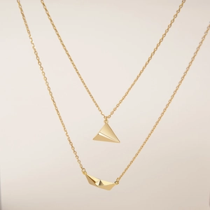 Minimalist layered gold necklace featuring origami airplane and paper boat pendants