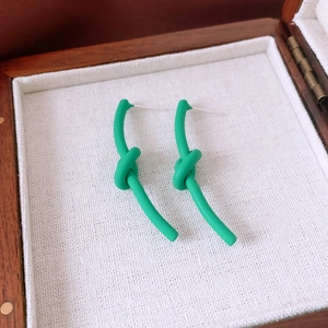 Detail view of green knotted earrings with matte lacquer finish on a premium display box