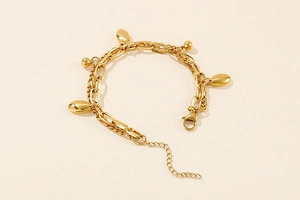 Detail eines goldfarbenen zweilagigen Armbands mit ovalem Anhänger und Karabiner