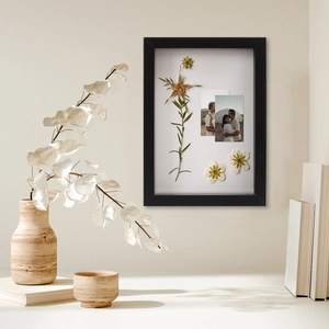Detail view of a black shadow box frame featuring dried flowers and polaroid photos