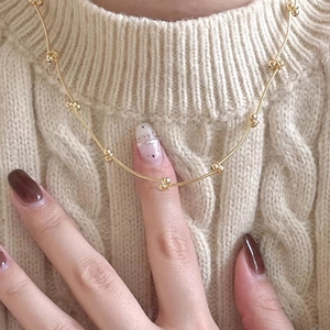 Close-up of minimalist gold beaded necklace worn over a beige knit sweater