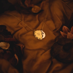 Golden sun and moon face pendant necklace displayed on vintage gold silk fabric background