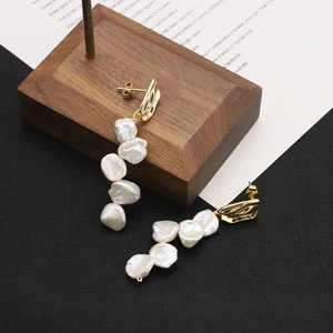 Elegant gold-tone long earrings with white baroque pearls shown on a display stand