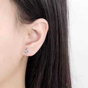 Minimalist silver four-pointed star stud earring with center crystal on model's ear