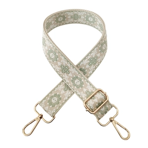 Detail of adjustable canvas strap with green and white floral embroidery and gold metal clips