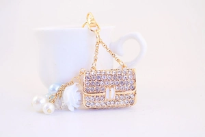 Detail of a golden handbag keychain with rhinestones, pearls, and a white rose charm