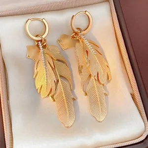 Detailed close-up of golden feather earrings with micro-inlaid diamonds on satin