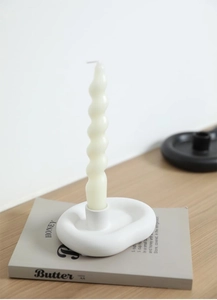 Minimalist cream ceramic donut candle holder with spiral taper candle on a book