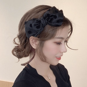 Elegant black velvet polka dot headband with a large bow shown on a female model