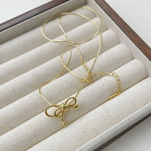 Detail of a golden bow pendant necklace with adjustable chain on a beige velvet display box