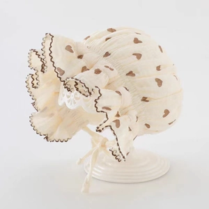 Détail d'un béguin pour bébé avec motifs de cœurs bruns et bords à volants en crème