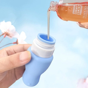 Filling a blue silicone travel bottle with shower gel against a floral sky background