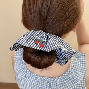 Détail du chouchou à carreaux bleus avec broderie cerise sur une coiffure en chignon